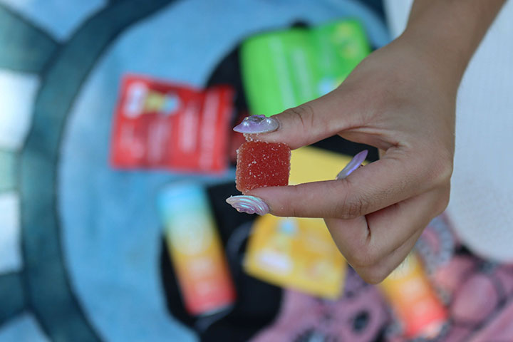 Woman holding THC edible over picnic blanket with cannabis products.